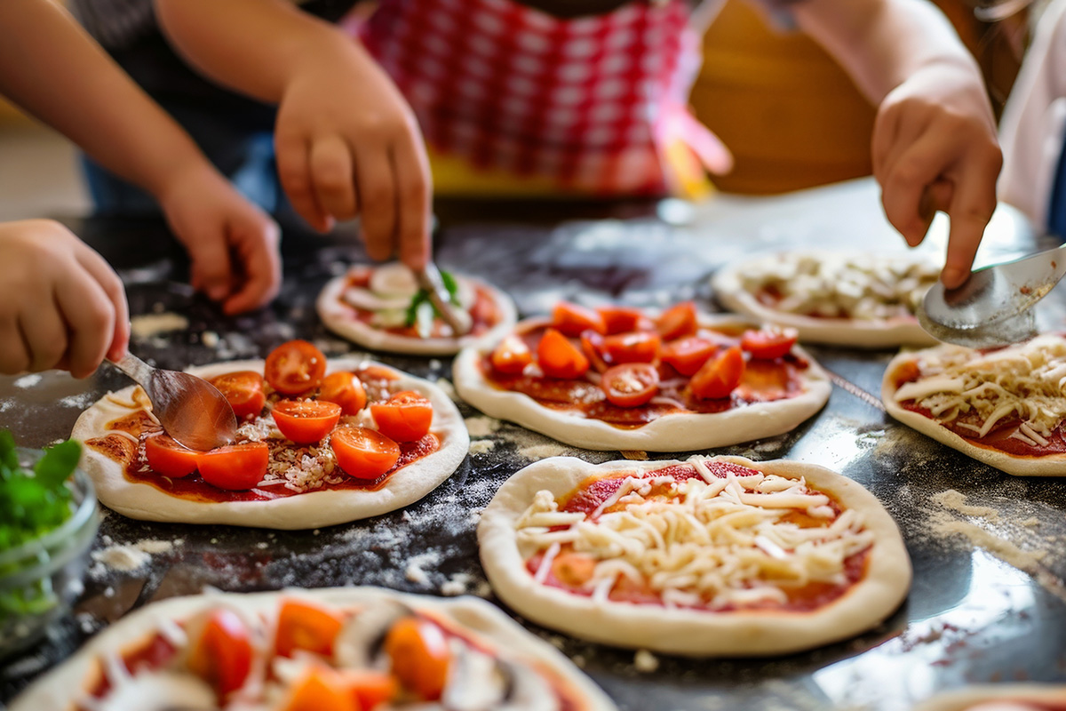 Kleine Hände belegen kleine Pizzen mit Tomaten, Käse und Gemüse.